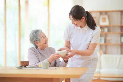 職員が高齢者に食事を提供する介護風景。温かい関わりが伝わります。